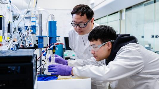 Two researchers wearing safety glasses and white lab coats using lab equipment